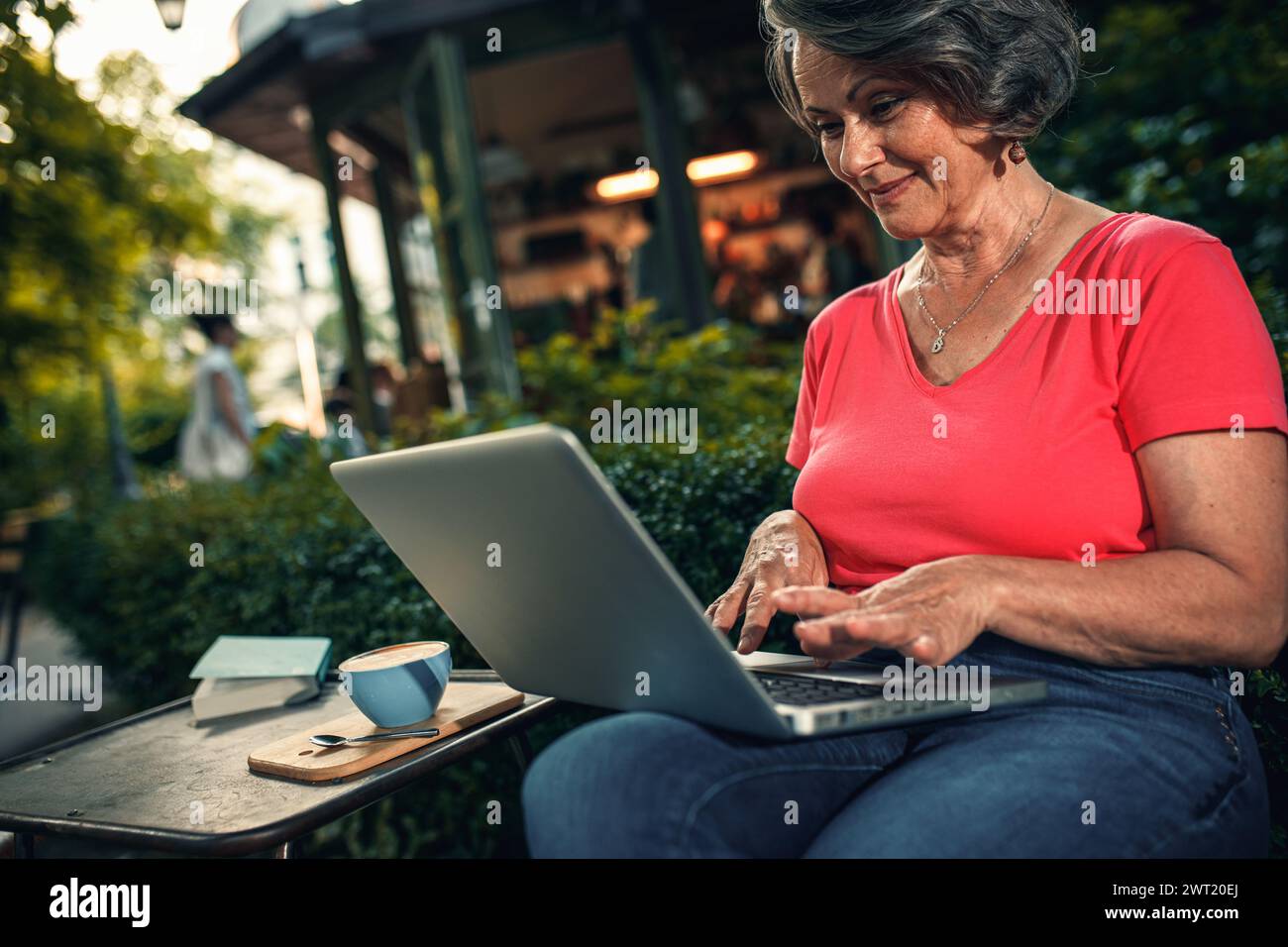 Ältere Frau, die im Café im Freien sitzt und einen Laptop benutzt und Kaffee trinkt. Stockfoto