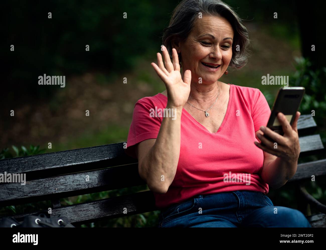 Ältere Frau, die im Park ein Handy benutzt. Stockfoto