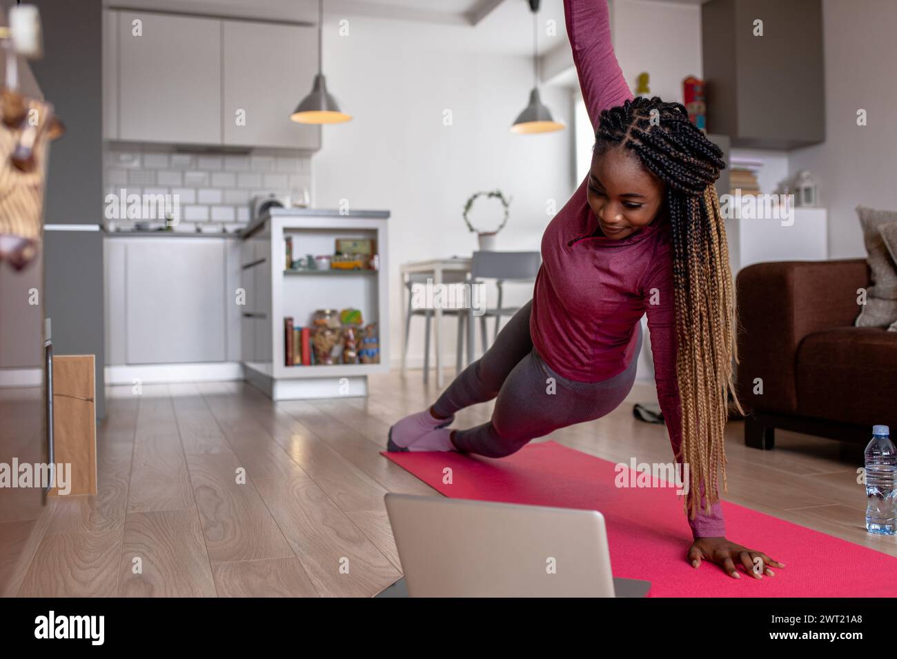 Junge afroamerikanische Frau zu Hause, die vor einem geöffneten Laptop Sport macht und Anweisungen eines professionellen Online-Fitnesstrainers wiederholt. Stockfoto