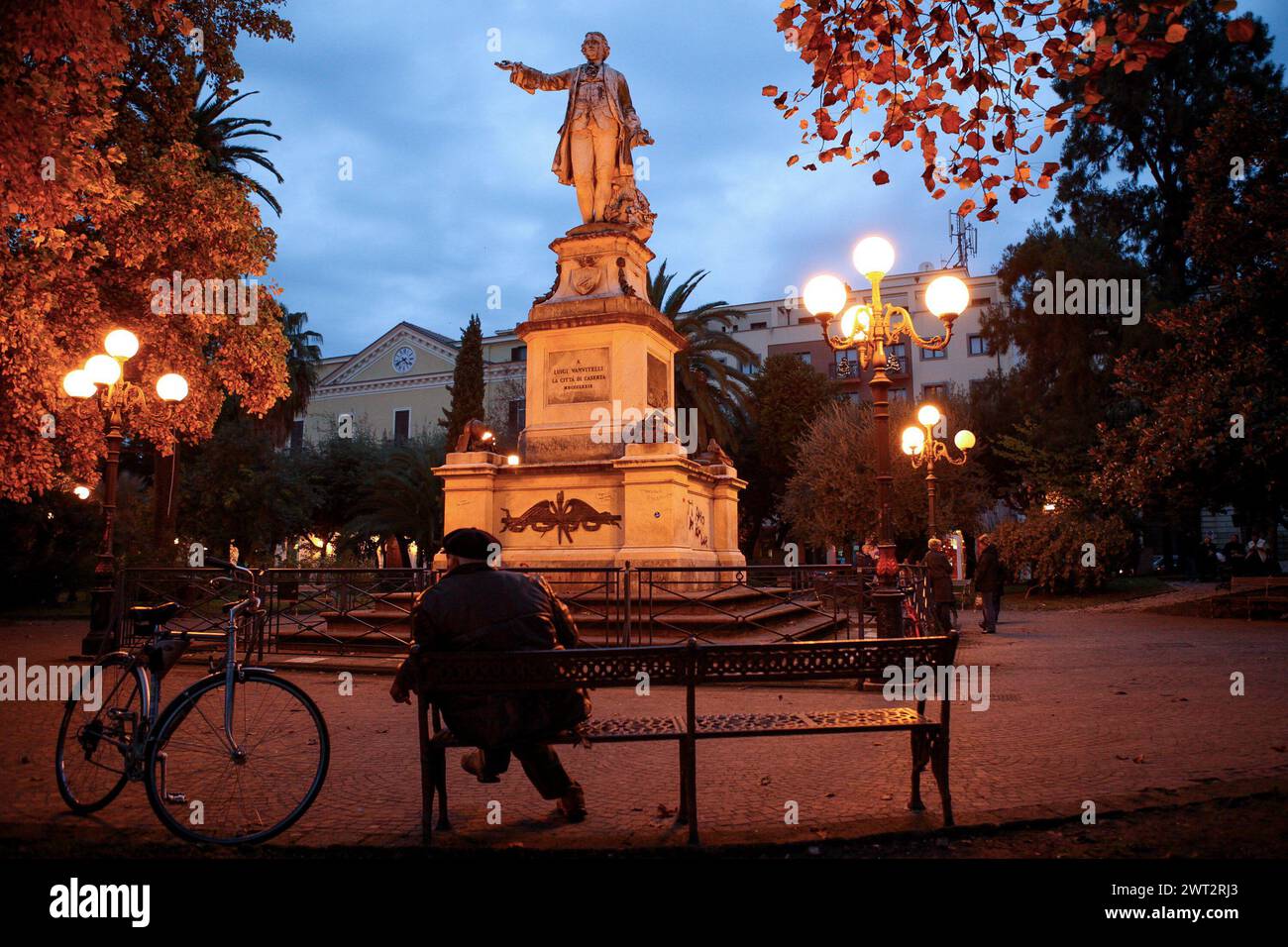 Ein Mann, der auf einer Bank auf dem Vanvitelli-Platz in Caserta sitzt. Vor ihm die Statue des Architekten Luigi Vanvitelli Stockfoto