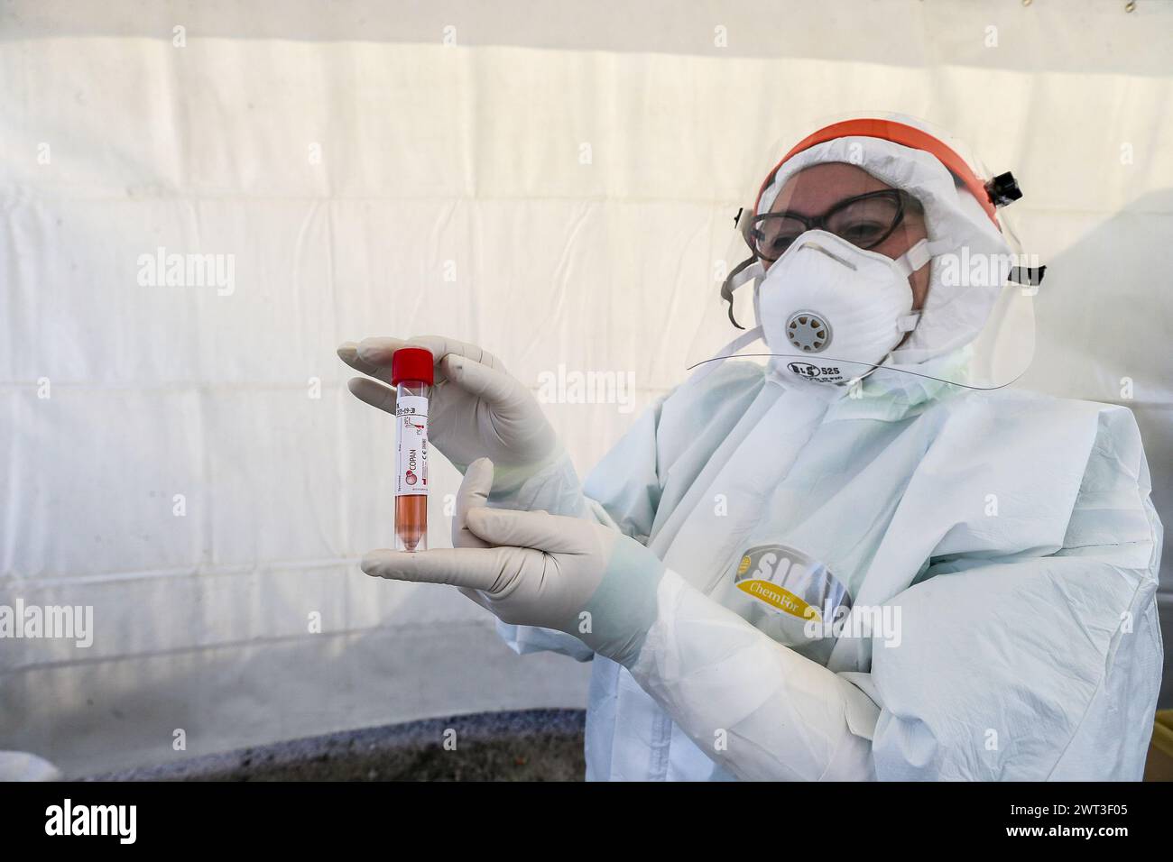 Ein Arzt, der sich in Overall und Masken zum Selbstschutz kleidet, zeigt das Reagenzglas für Personen, die den Test auf das Coronavirus COVID-19 durchführen müssen; Stockfoto