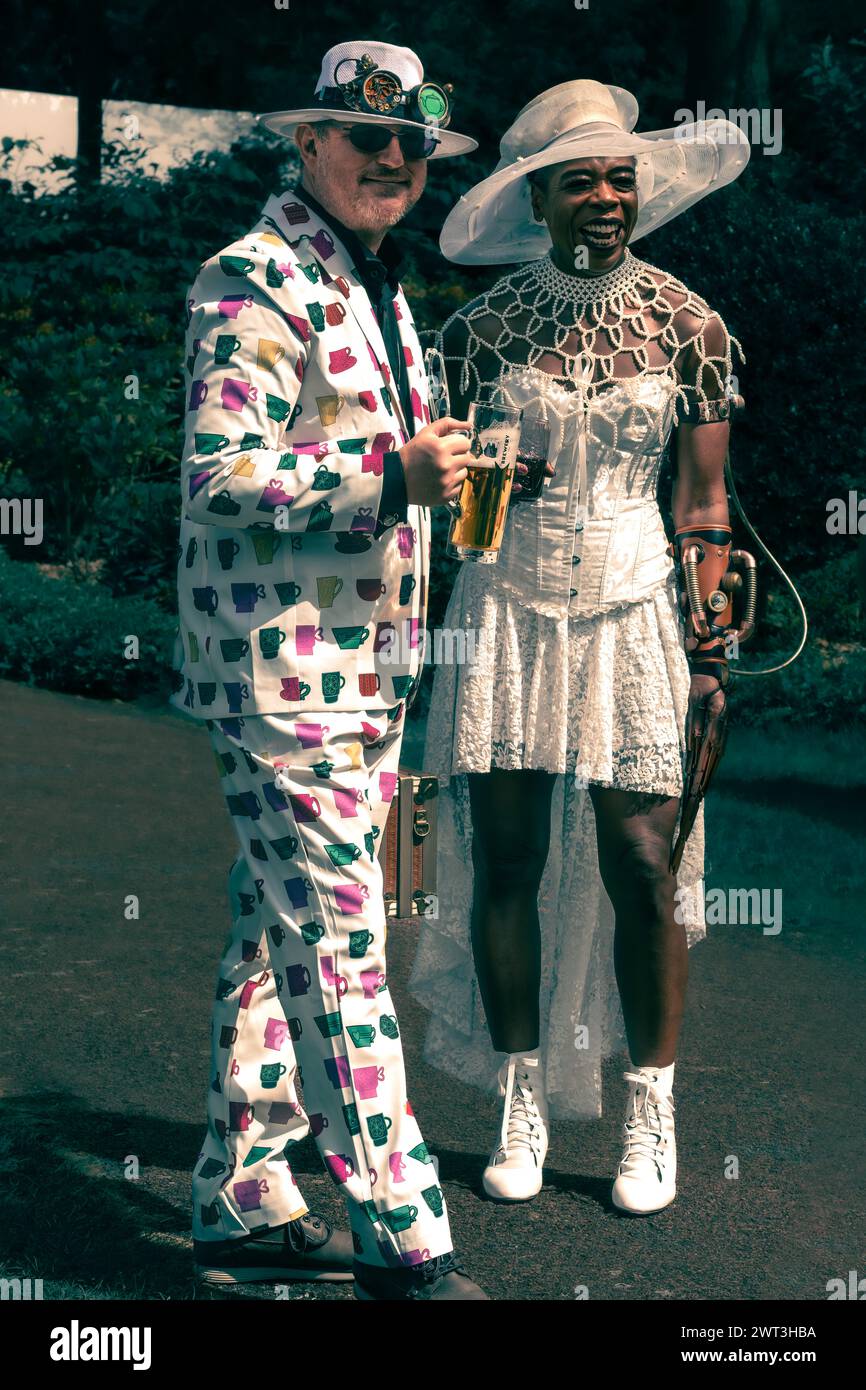 Zwei farbenfrohe Steam Punk-Leute in bunten Kostümen mit Hüten und Getränken Stockfoto