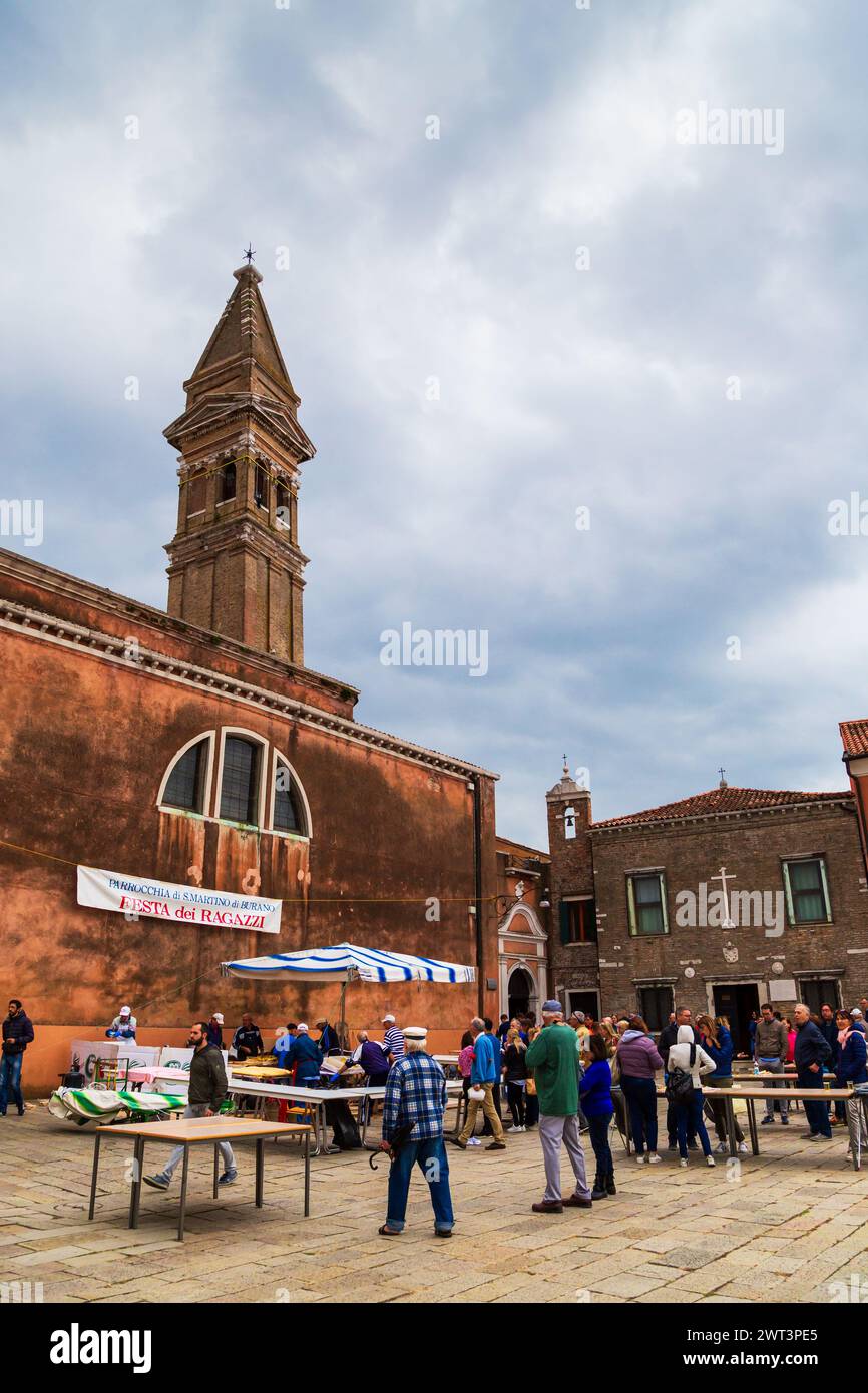 Burano, Italien - 6. Oktober 2019: Touristen auf der Stadtmesse, dem Hauptplatz von Burano, Piazza Galuppi. Berühmter Schiefer Glockenturm Campanile Pendente der Bischofskirche Saint Martin auf Burano, Venedig, Italien. Stockfoto