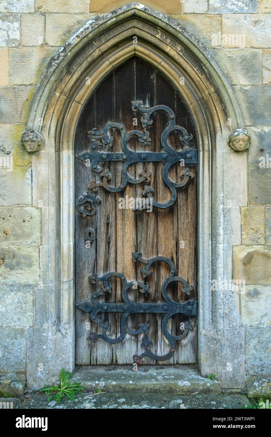 Detail einer Seitentür der Burton Agnes Church mit verwittertem Holz und extravaganten Eisenarbeiten. Stockfoto