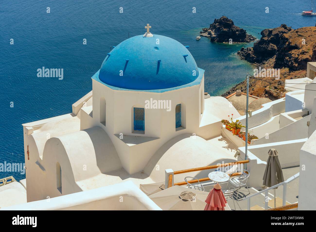 Vor der blauen Ägäis ist eine berühmte Kapelle mit blauer Kuppel abgebildet, die typisch für viele auf der Caldera von Santorin zu finden ist. Stockfoto