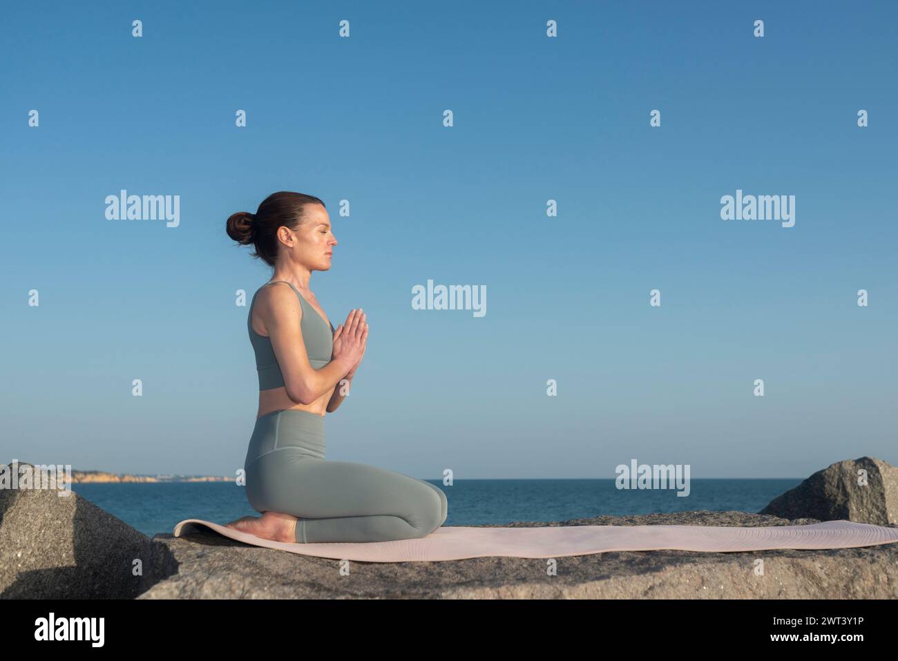 Frau kniet auf einer Yogamatte und meditiert am Meer. Stockfoto