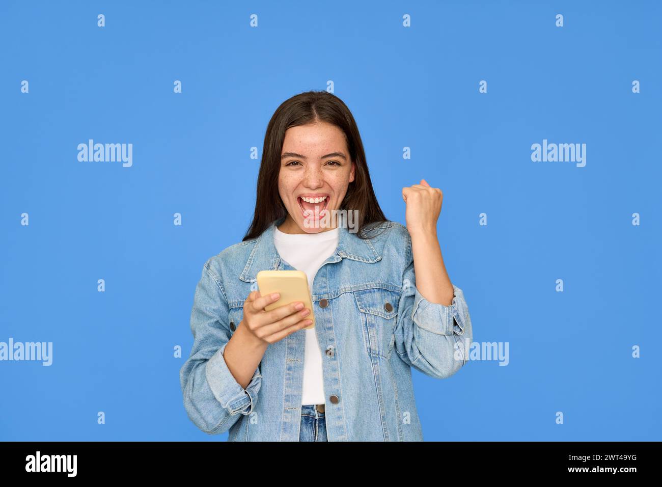 Aufgeregt Gen z Latin Girl feiert Sieg mit Handy im Hintergrund. Stockfoto