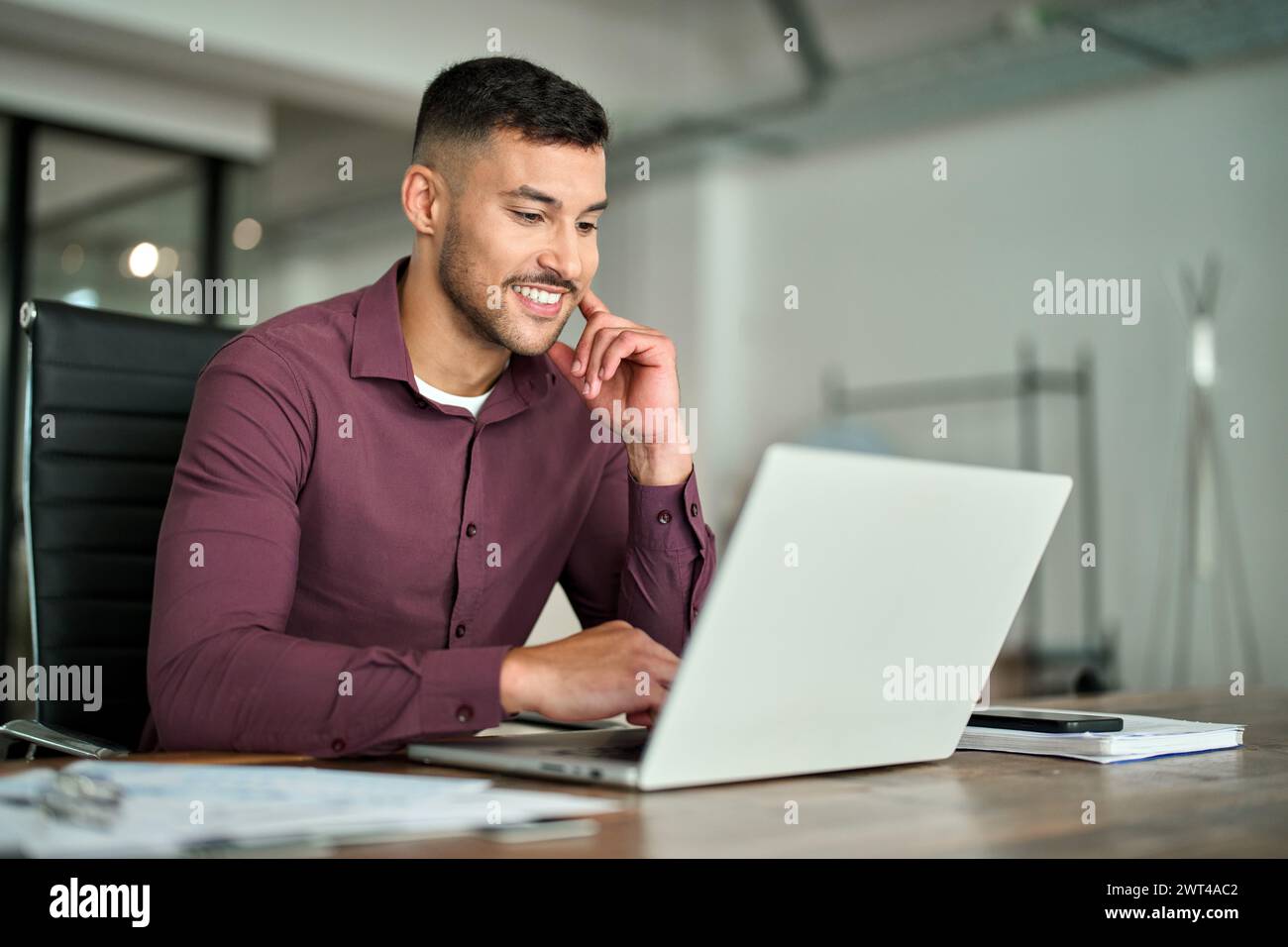 Glücklicher, beschäftigter Geschäftsmann aus Lateinamerika, der am Laptop arbeitet und am Schreibtisch im Büro sitzt. Stockfoto