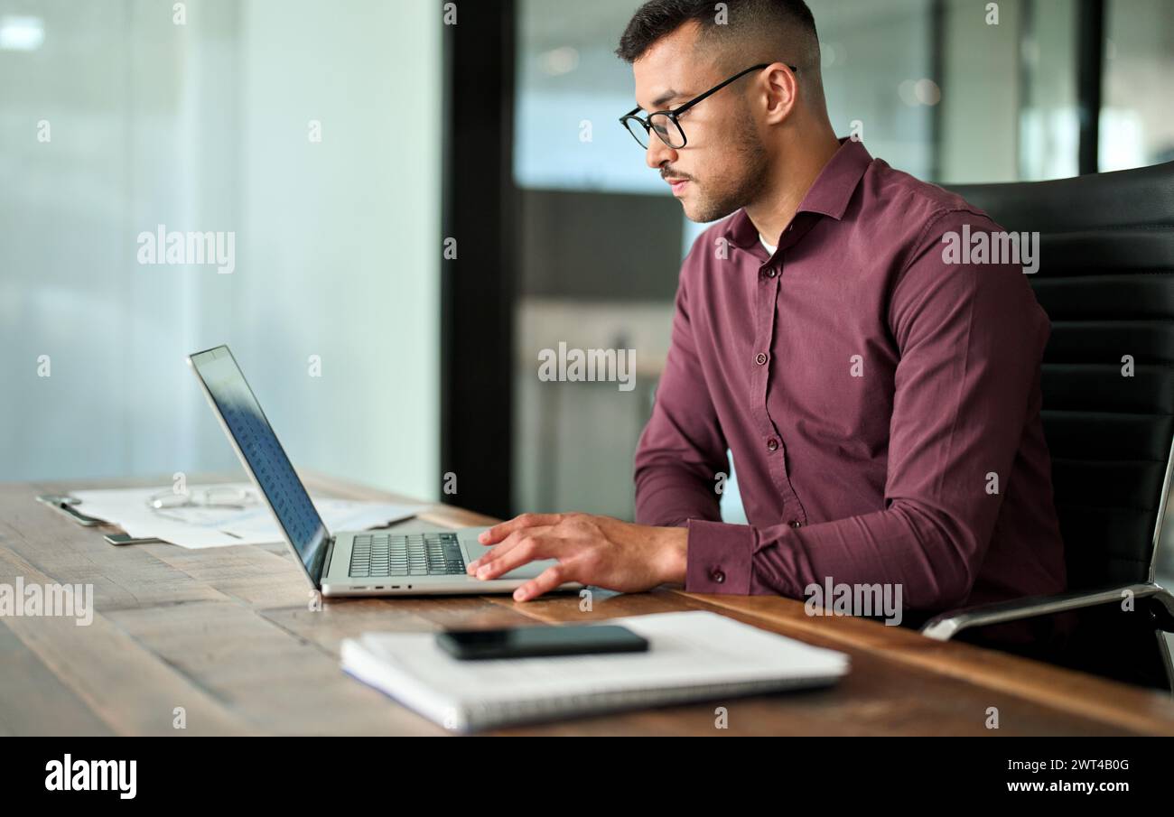 Geschäftiger, junger Geschäftsmann aus Lateinamerika, der am Laptop arbeitet und am Schreibtisch sitzt. Stockfoto