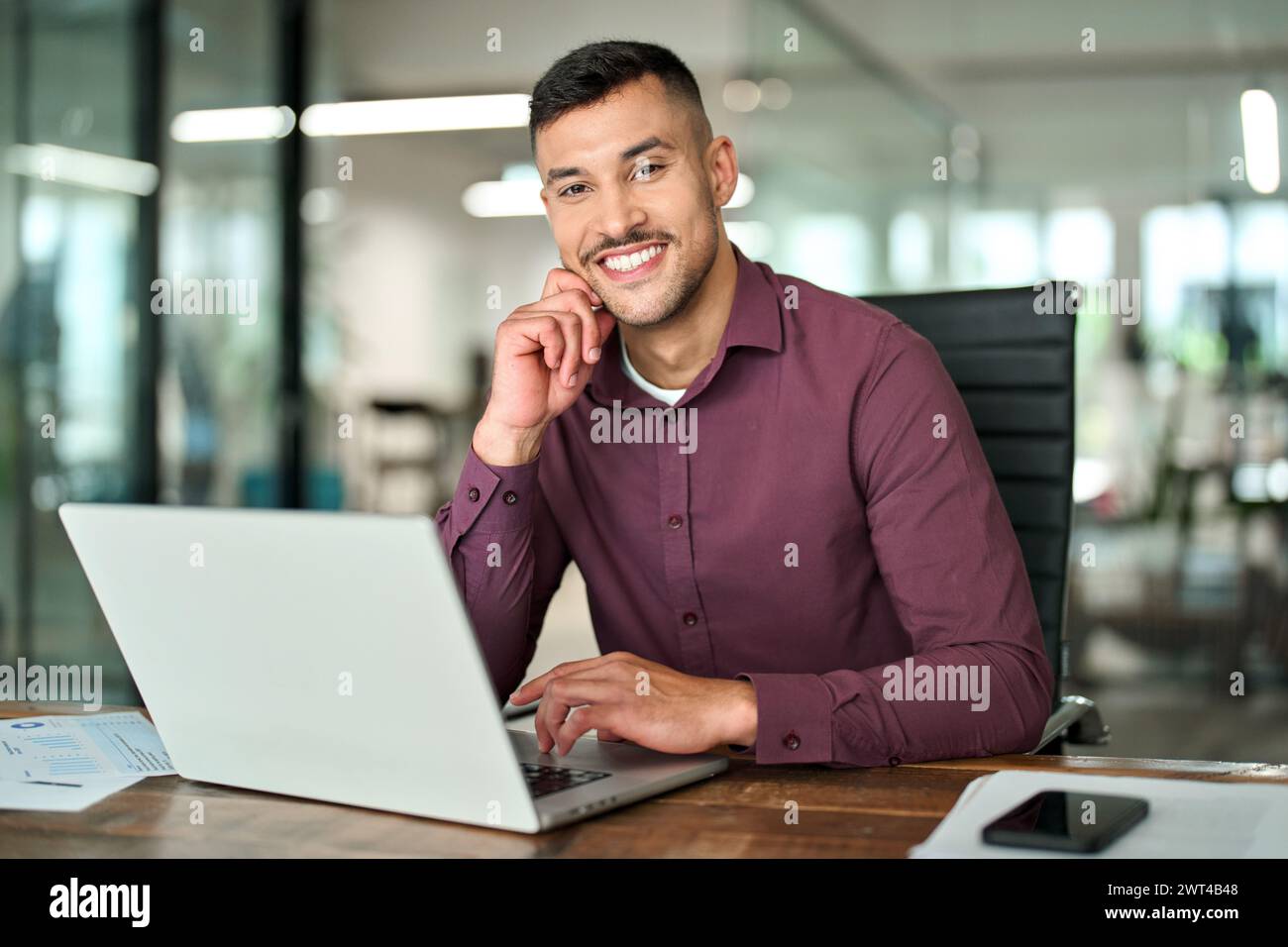 Glücklicher professioneller lateinamerikanischer Geschäftsmann, der bei der Arbeit auf die Kamera schaut, Porträt. Stockfoto