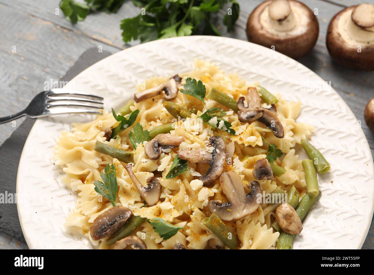 Vegetarische Pasta mit Pilzen, Petersilie, Bohnen und Käse auf grauem Holztisch, Nahaufnahme Stockfoto