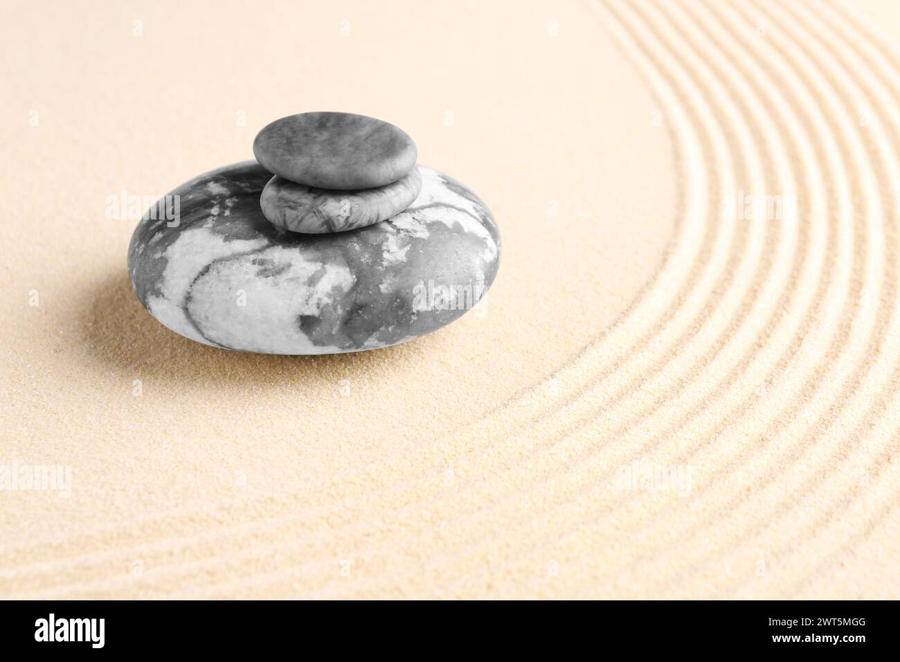 Zen-Gartensteine auf beigem Sand mit Muster. Leerzeichen für Text Stockfoto