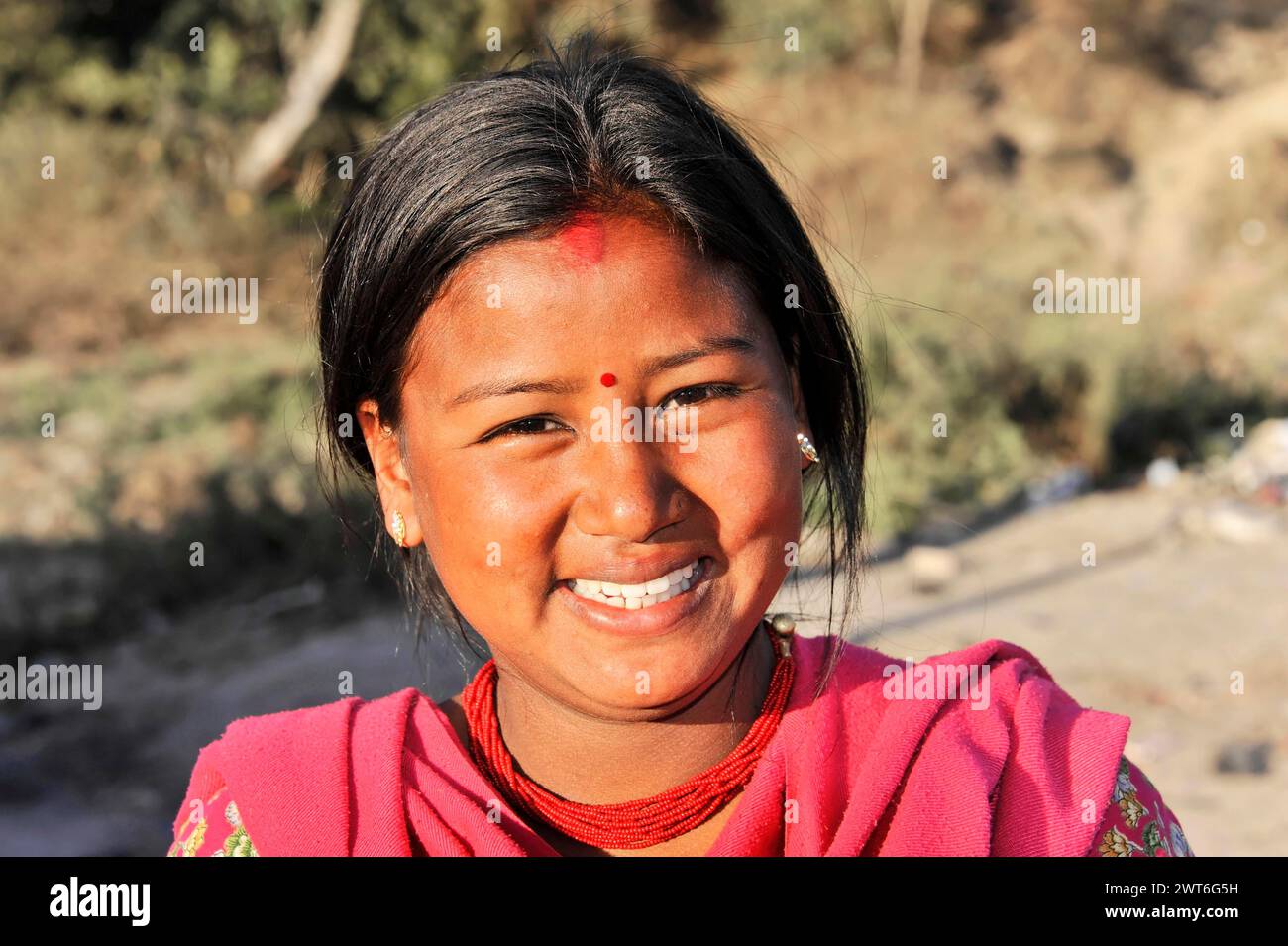 Ein junges Mädchen lächelt breit in der Sonne mit einem roten Bindi auf der Stirn, Kathmandu Valley. Kathmandu, Nepal Stockfoto