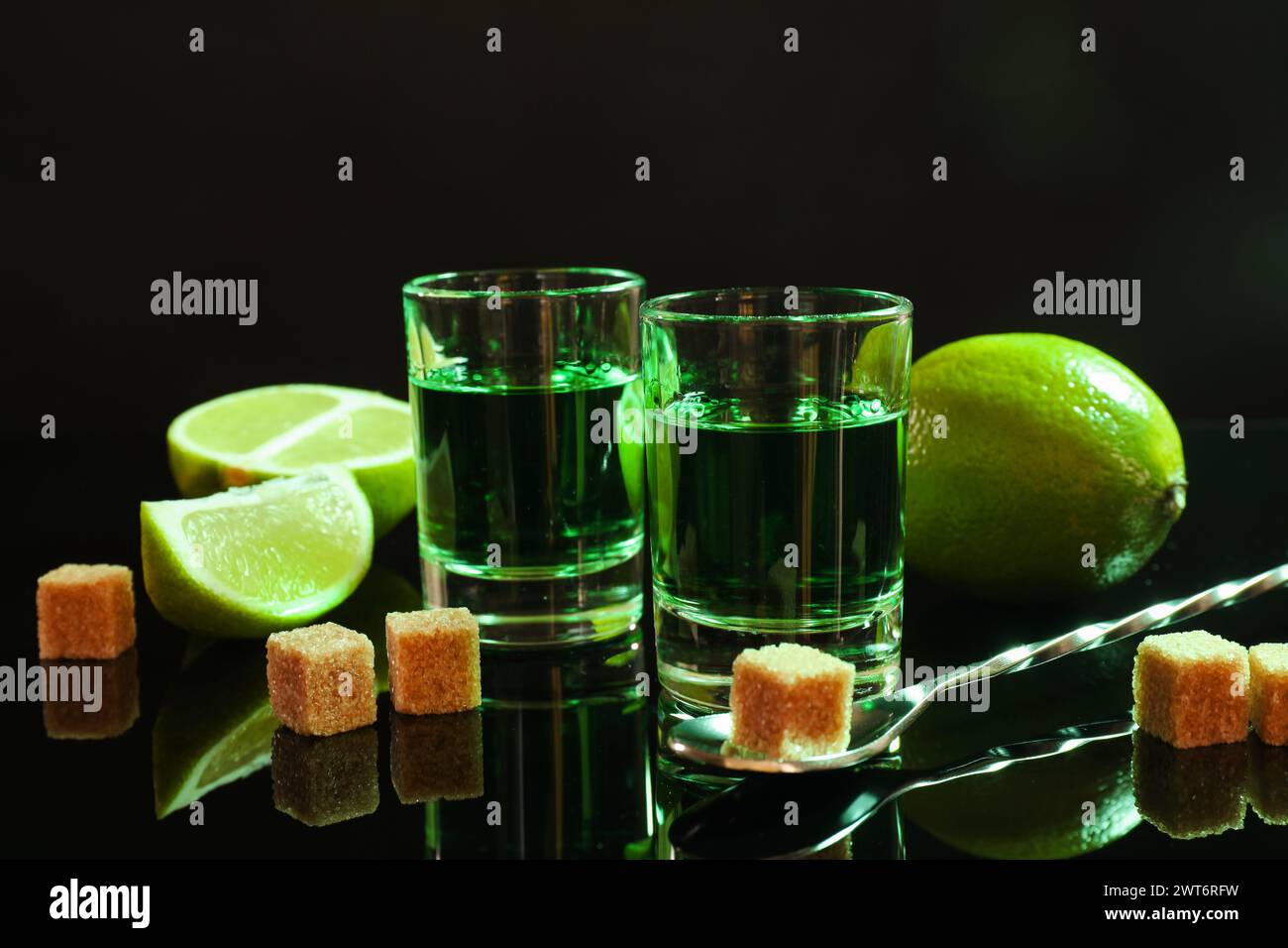 Absinth in Gläsern, brauner Zucker, Limette und Löffel auf Spiegeltisch. Alkoholisches Getränk Stockfoto