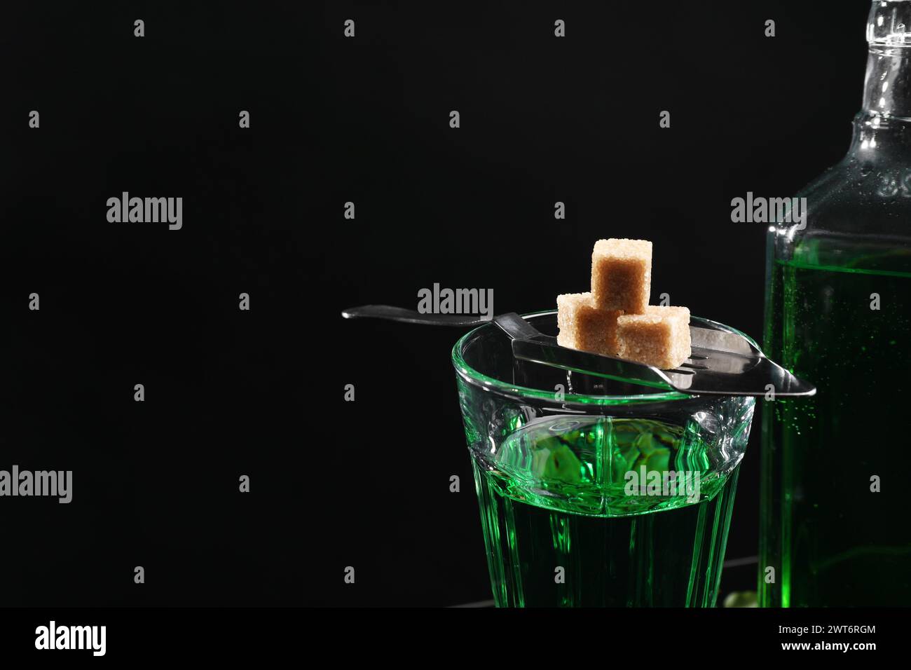 Absinth in Glas, brauner Zucker und Löffel vor schwarzem Hintergrund, Textraum. Alkoholisches Getränk Stockfoto