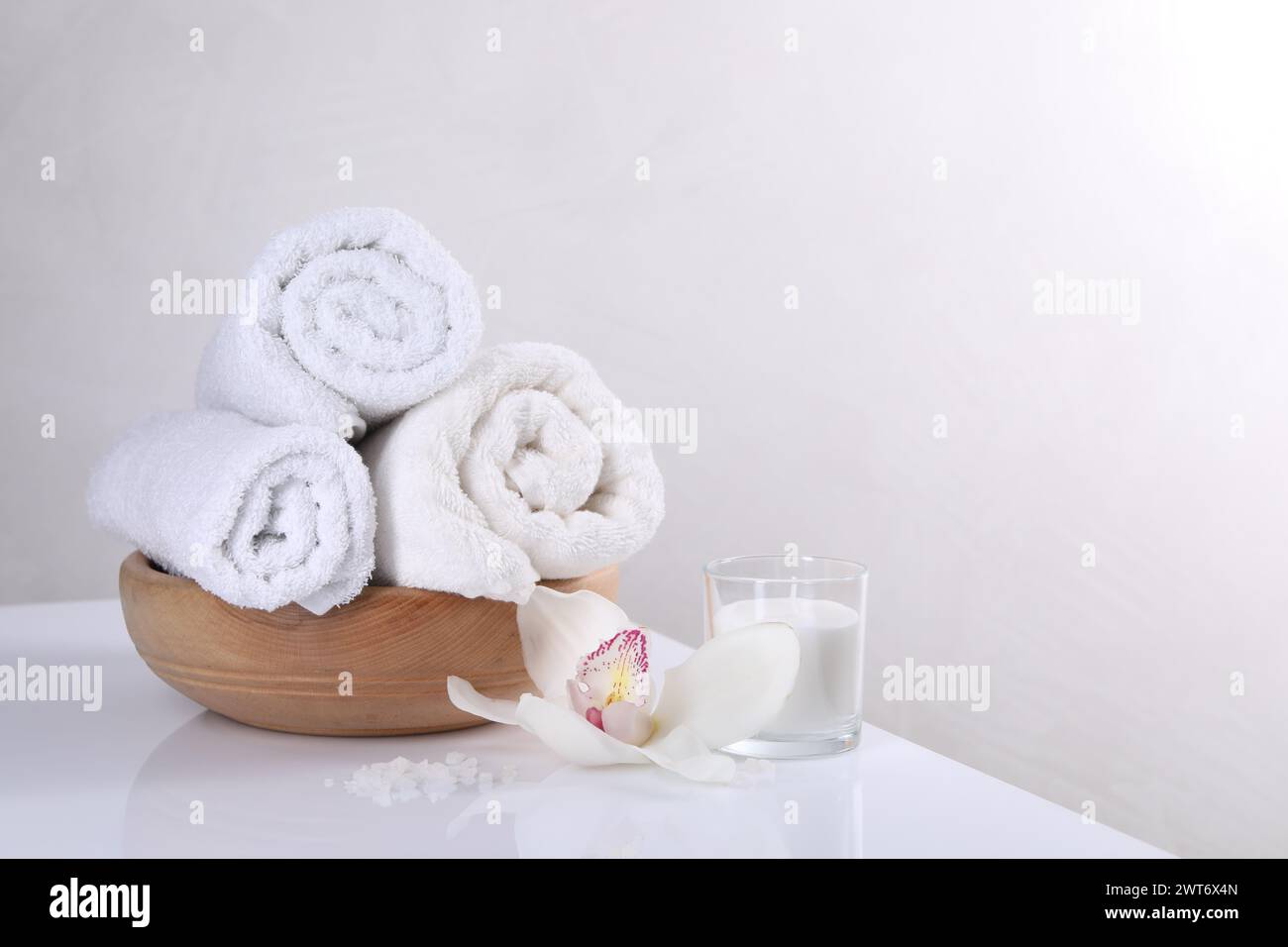 Spa-Komposition mit Handtüchern, Orchideenblume, Kerze und Meersalz auf weißem Tisch, Platz für Text Stockfoto