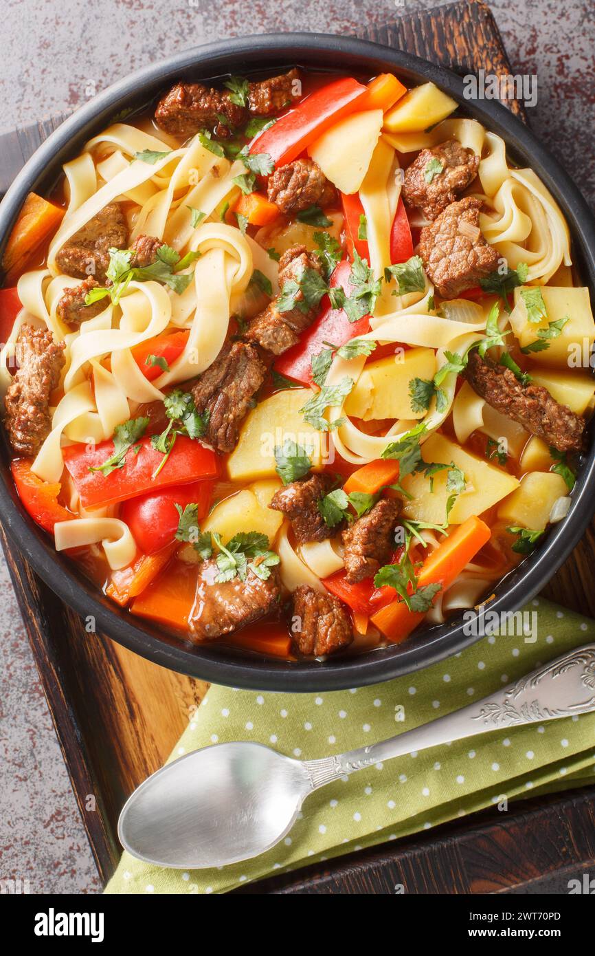 Laghman-Nudelsuppe aus Usbekistan mit Rinderfutter, Tomatenpaste, Gemüse und Kräutern aus der Nähe auf dem Teller auf dem Holzbrett. Vertikal oben VI Stockfoto