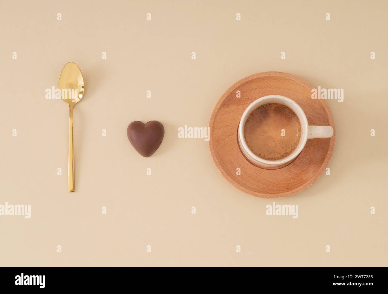 Ich liebe Kaffee. Kreative Komposition mit goldenem Löffel, Schokoladenherz und einer Tasse Kaffee auf pastellfarbenem beigem Hintergrund. Minimales Konzept. Stockfoto