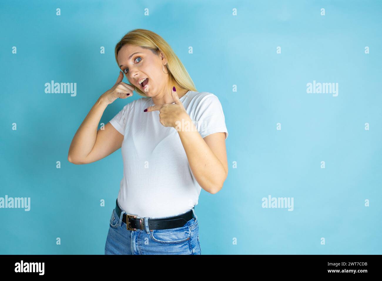 Junge schöne Frau, die ein lässiges T-Shirt über isoliertem blauem Hintergrund trägt und die „Call me“-Geste mit ihren Händen macht. Stockfoto