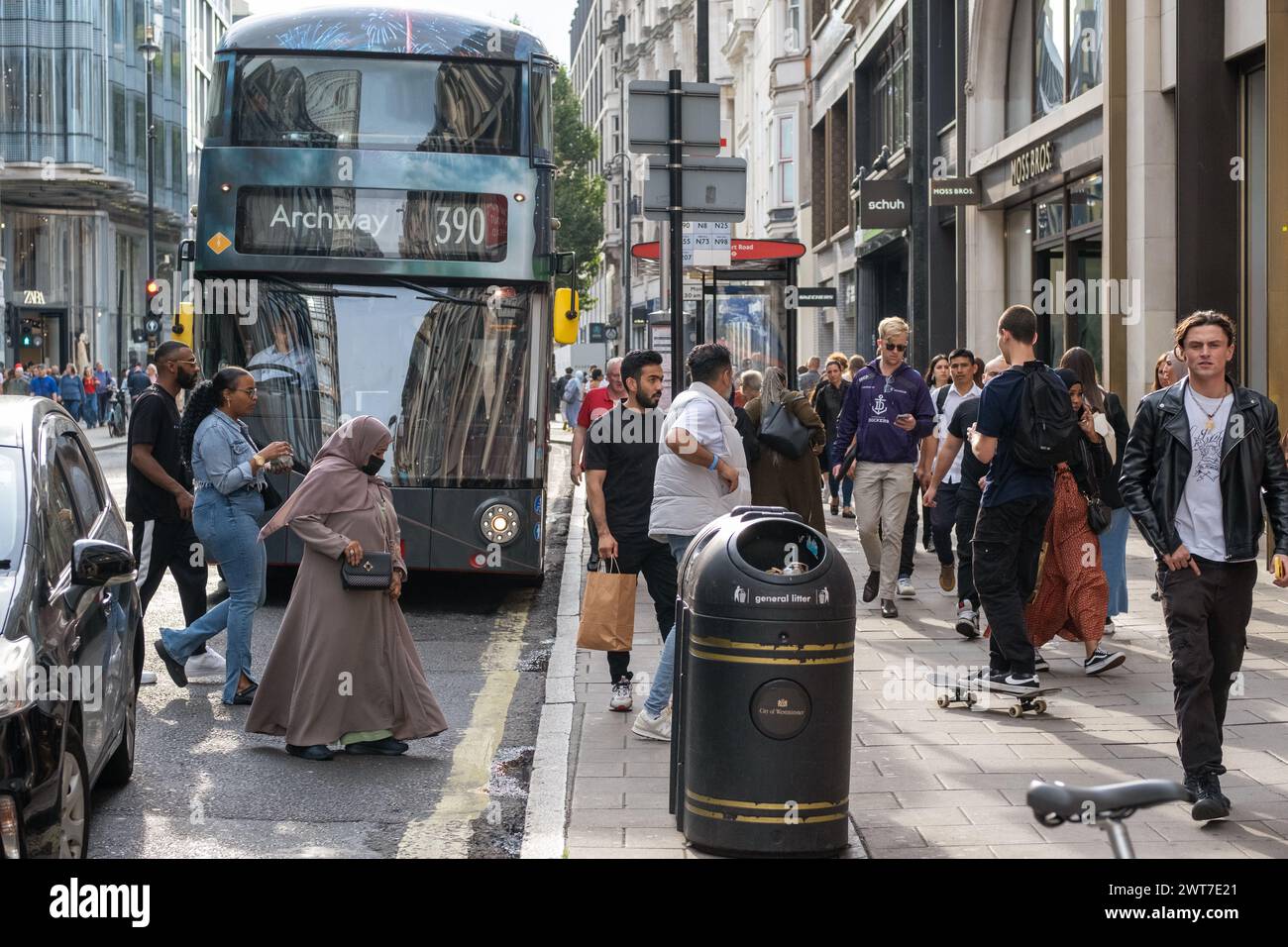Der Bus 390 an einer Bushaltestelle in der Oxford Street, London. Die Szene ist voll mit Fußgängern, die die Straße überqueren und an den Geschäften vorbeilaufen. Stockfoto