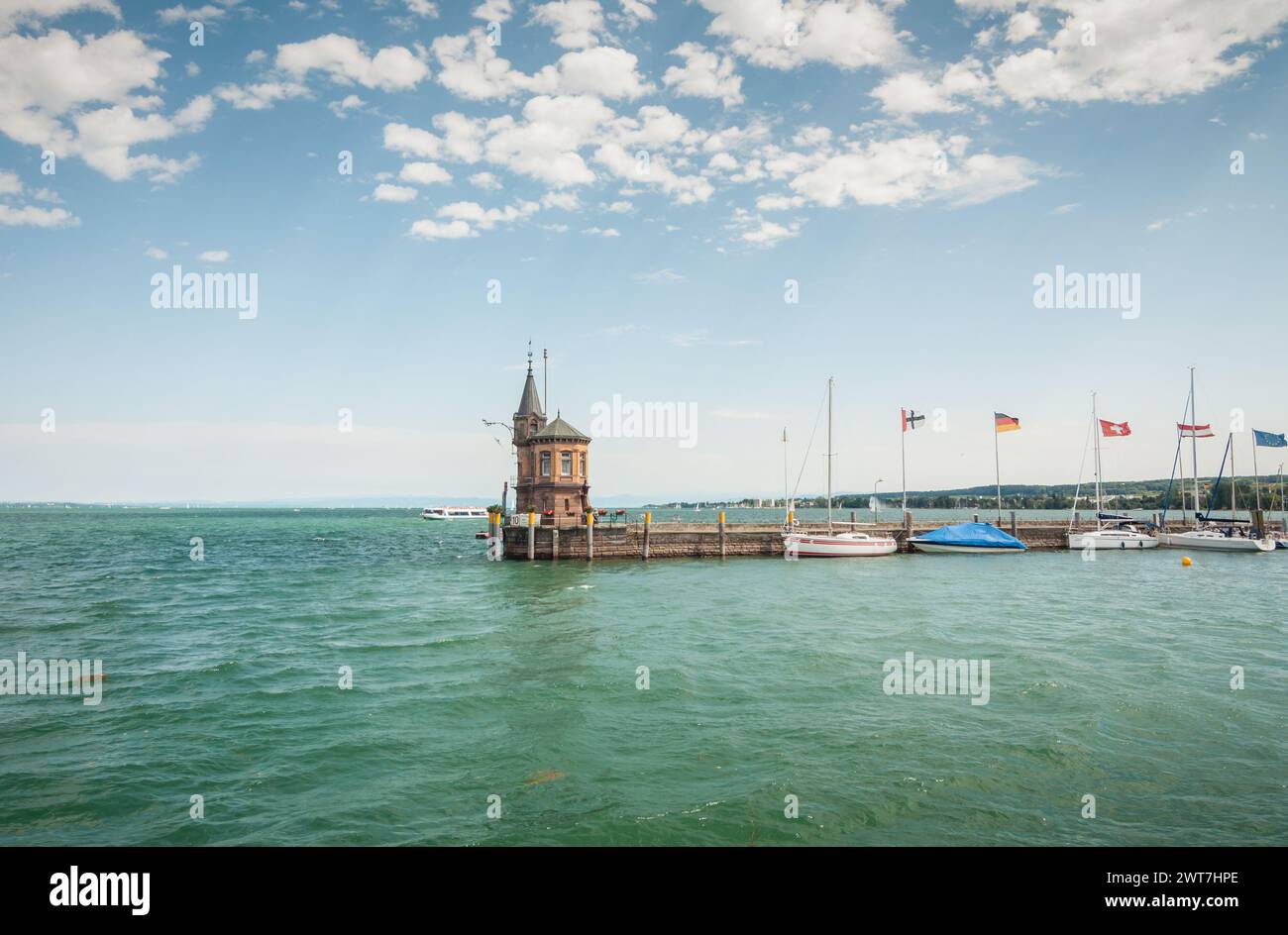 Alter Leuchtturm am Ende des Steinmole im Konstanzer Hafen. Nur wenige Segelboote liegen am Pier. Wunderschöner Blick auf den Bodensee, blauer Himmel hinten. Stockfoto