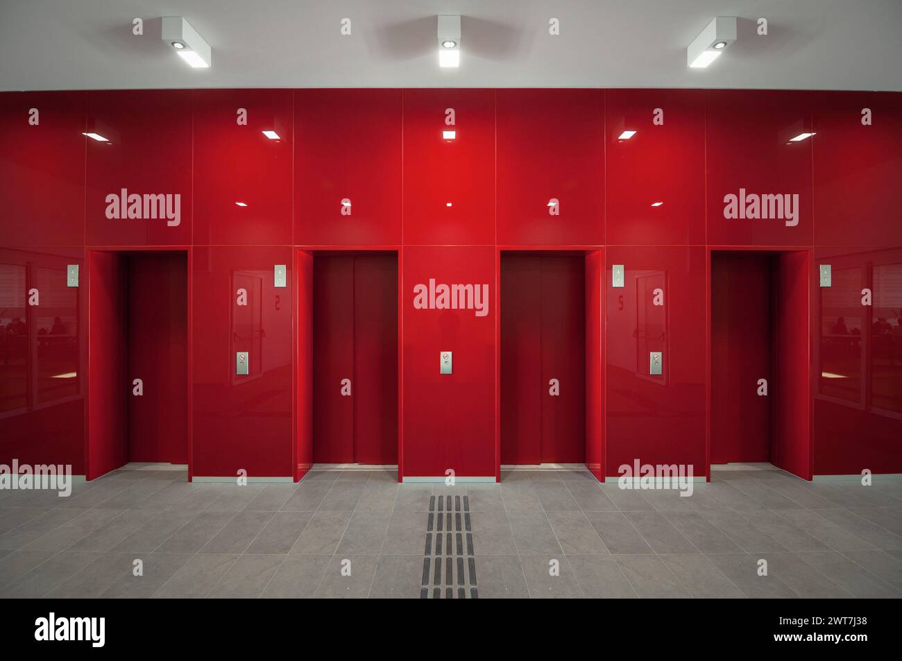 Vier Aufzugstüren in einer roten Wand. Zweidimensionales Bild der glänzend roten Wand im ersten Stock mit taktiler Markierung. Leere Innenlobby des neuen Gebäudes. Stockfoto