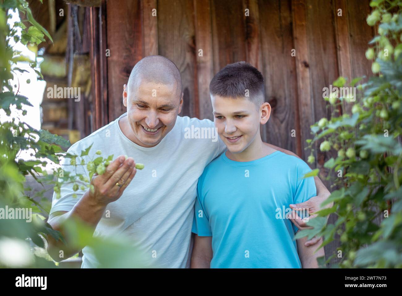 Ein Mann und ein Junge, Vater und Sohn, teilen einen Moment der Freude, während sie Pflanzen in einem Garten vor einer hölzernen Kulisse, Familie Binding Zeit und Gesundheit in Stockfoto