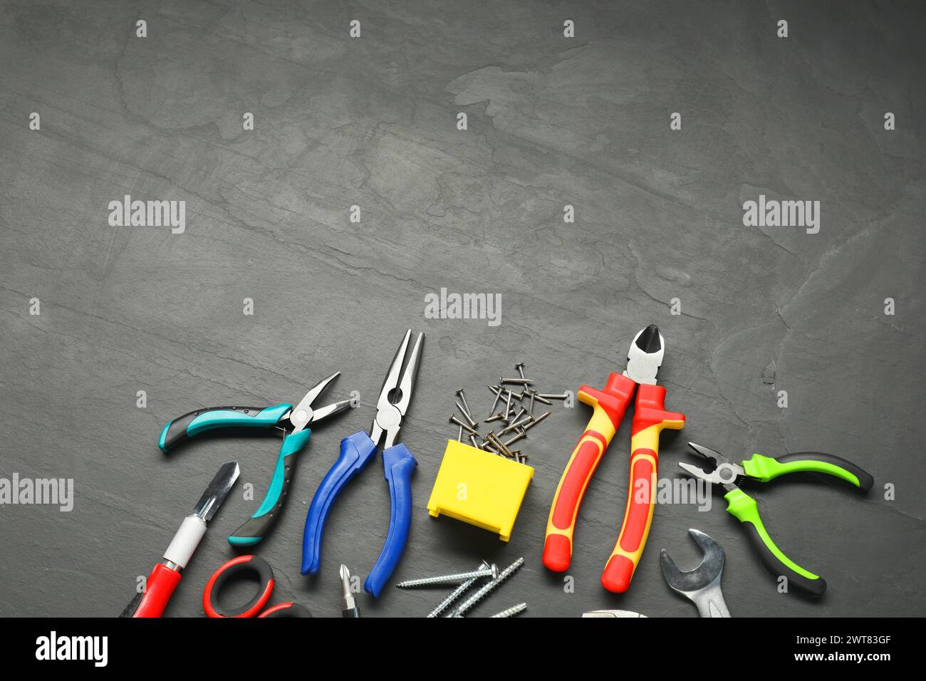 Verschiedene Zangen, Schraubenschlüssel, Nägel und andere Reparaturwerkzeuge auf schwarzem, strukturiertem Tisch, flache Lagen. Leerzeichen für Text Stockfoto