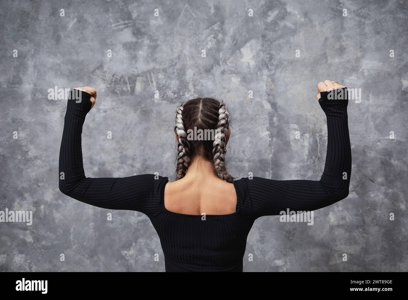 Eine athletische Frau trainiert in der Nähe einer Wand, steht mit dem Rücken zur Kamera, beugt ihre Arme im rechten Winkel und spreizt sie zur Seite, Kraft Stockfoto