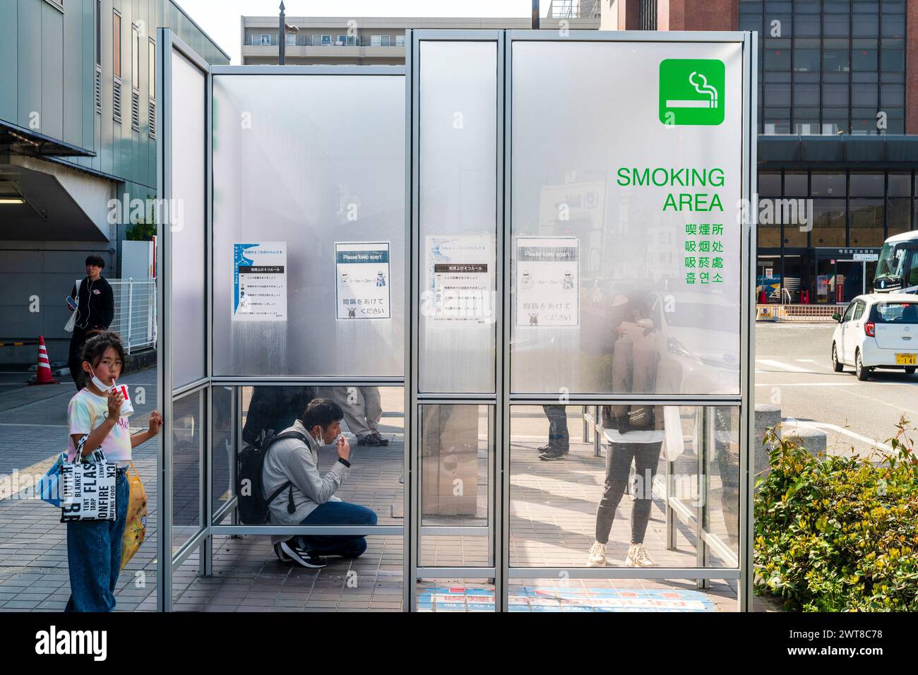 Ausgewiesener Raucherbereich auf der Straße vor dem Bahnhof in Akashi City in Japan. Ein matter Bildschirm, der das Rauchen mit etwas Privatsphäre bietet. Stockfoto