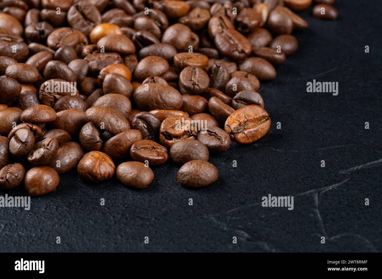 Geröstete Kaffeebohnen in einer großen Pfanne auf dunklem Hintergrund verstreut Stockfoto