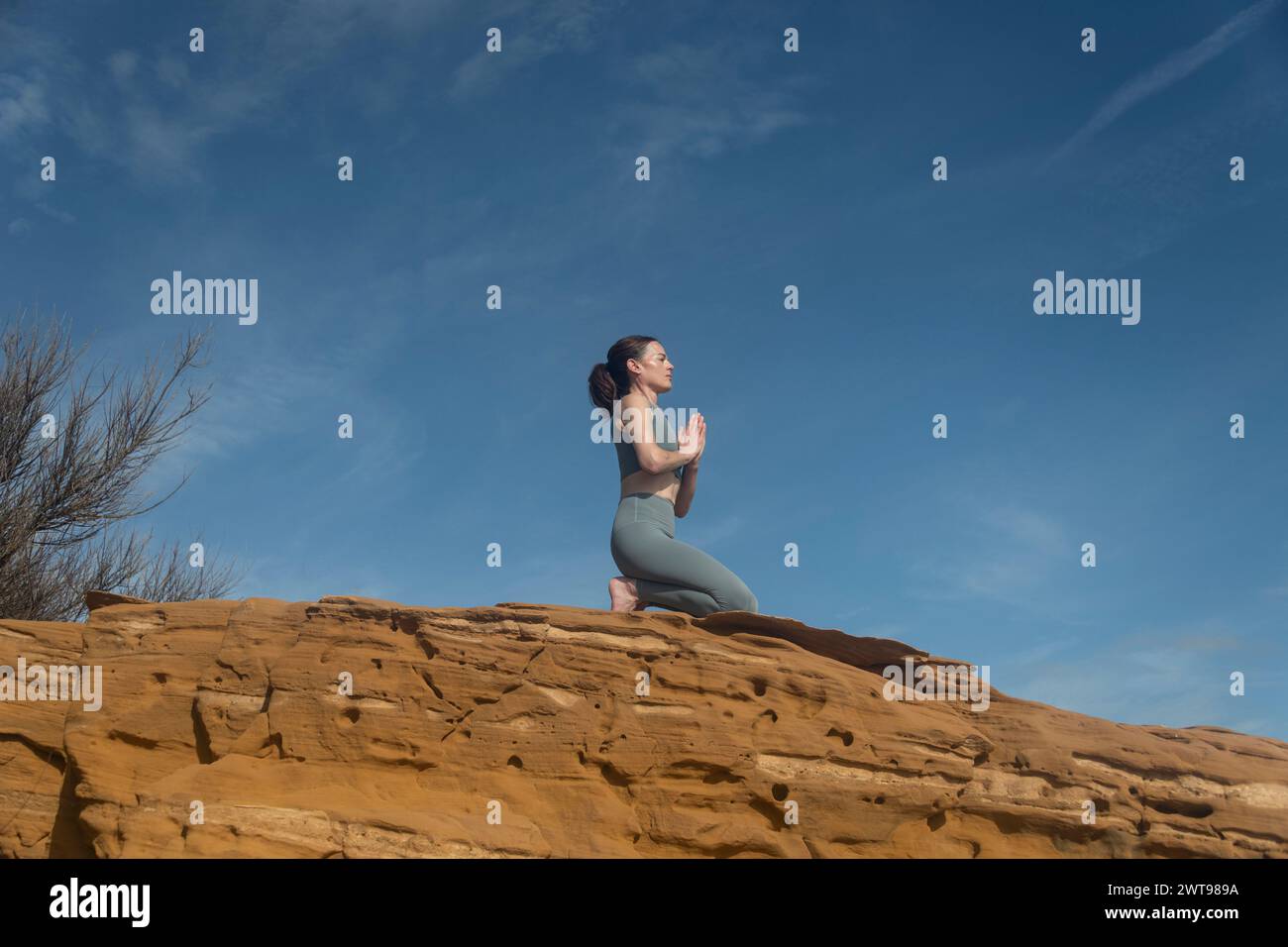 Frau, die draußen auf roten Felsen kniet, meditiert und Yoga praktiziert. Gelassenheit Stockfoto