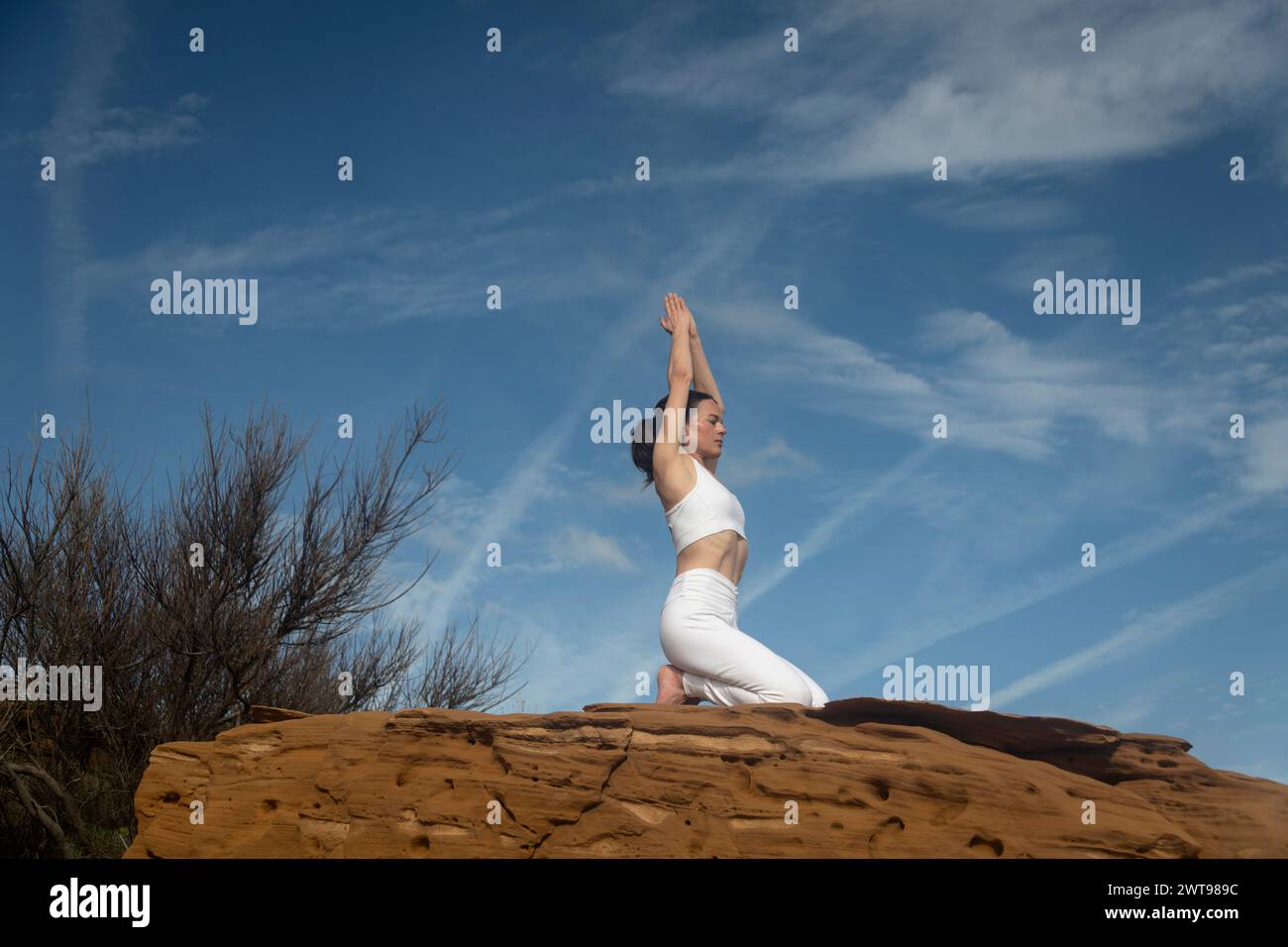 Frau, die draußen auf roten Felsen kniet, meditiert und Yoga praktiziert. Gelassenheit Stockfoto
