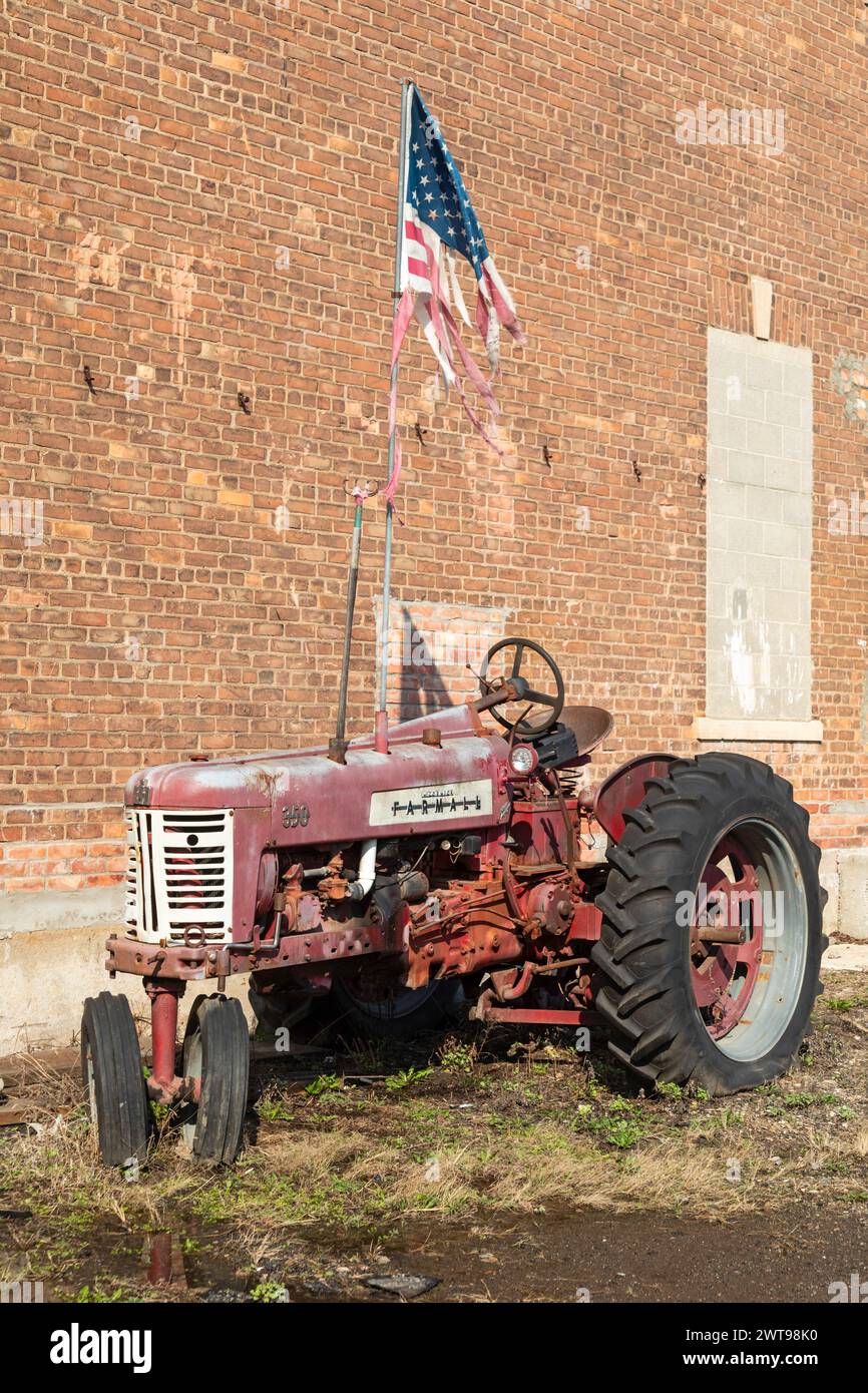 Detroit, Michigan - ein alter McCormick Farmall-Traktor fliegt vor einer Autowerkstatt eine zertrümmerte amerikanische Flagge. Stockfoto