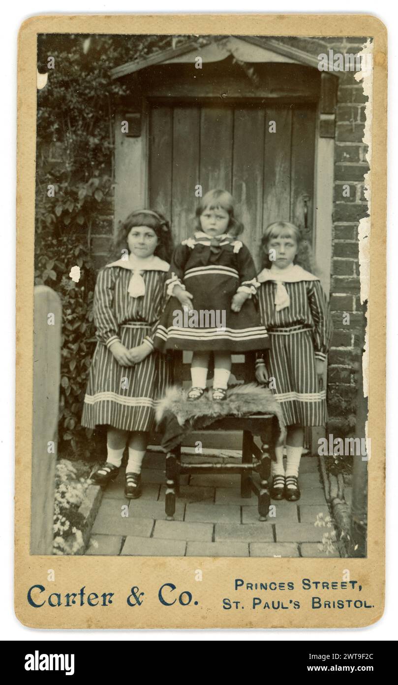 Originale viktorianische Karte (Visitenkarte oder CDV) 3 viktorianische Kinder vor der Haustür im Garten, im Sommer, in gestreiften Kleidern mit Matrosenanzügen, die zu dieser Zeit beliebt waren, weiße Socken und Riemensandalen. Aus dem Studio von Carter & Co. Princes Street, St. Paul's, Bristol. Um 1885. Stockfoto