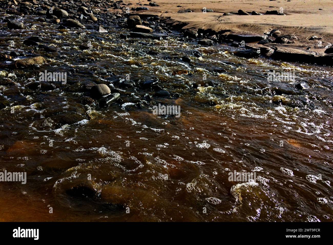 Eine Nahaufnahme von Wasser, das über Felsen fließt und die nassen Oberflächen unter hellem Licht beleuchtet. Stockfoto