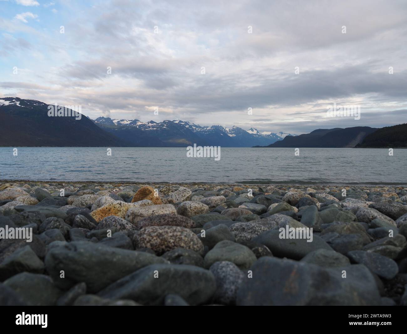 Malerische Haines, Alaska Küste, mit Kieselstein im Vordergrund, ruhigen Gewässern und majestätischen schneebedeckten Bergen unter einem bewölkten Himmel Stockfoto
