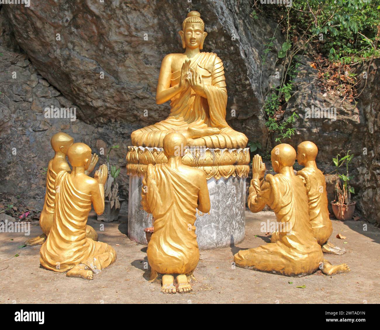 Buddha-Statue mit Mönchen, die beten. Der Buddhismus ist ein integraler Bestandteil des Lebens in Luang Prabang, der zum UNESCO-Weltkulturerbe gehört Stockfoto
