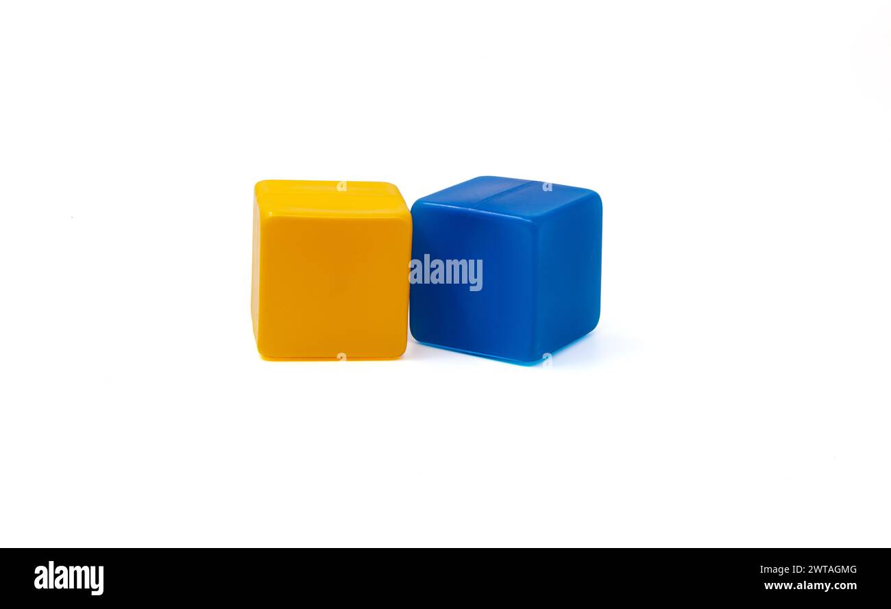 Mehrfarbige Plastikwürfel für Kinderspiele. Gelbe und blaue Würfel liegen nebeneinander. Weißer Hintergrund. Einer in der Nähe des anderen. Horizontal. Stockfoto