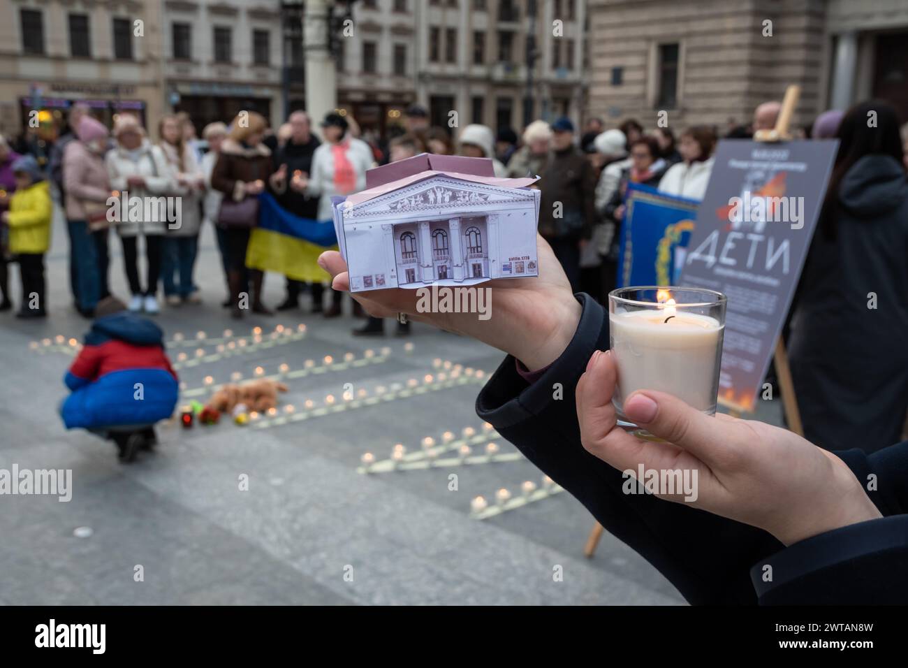 Blick auf Hände, die eine Kerze halten, und ein Modell eines Theaters, das während der Gedenkveranstaltung von den russischen Bomben getroffen wurde. Die Bewohner von Lwiw und die zwangsvertriebenen Bewohner des besetzten Mariupol nehmen an einer Veranstaltung zum Gedenken an die vor 2 Jahren verstorbenen Menschen im Mariupol-Theater in der Nähe des Nationalen Akademischen Operntheaters und Balletts von Solomiya Krushelnytska Teil. Die Bewohner von Mariupol versammelten sich in der Nähe der Theater von Lemberg und vieler Städte der Ukraine und zündeten Gedenklampen an, um an die Toten zu erinnern. Am 16. März 2022 warfen die russischen Besatzungsmitglieder Luftbomben auf die Theater im März Stockfoto