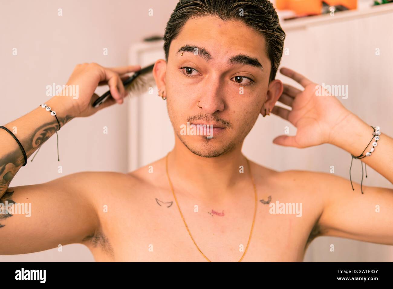 Ein junger Latino stylt aufmerksam seine Haare und reflektiert einen Moment des täglichen Frisierens Stockfoto