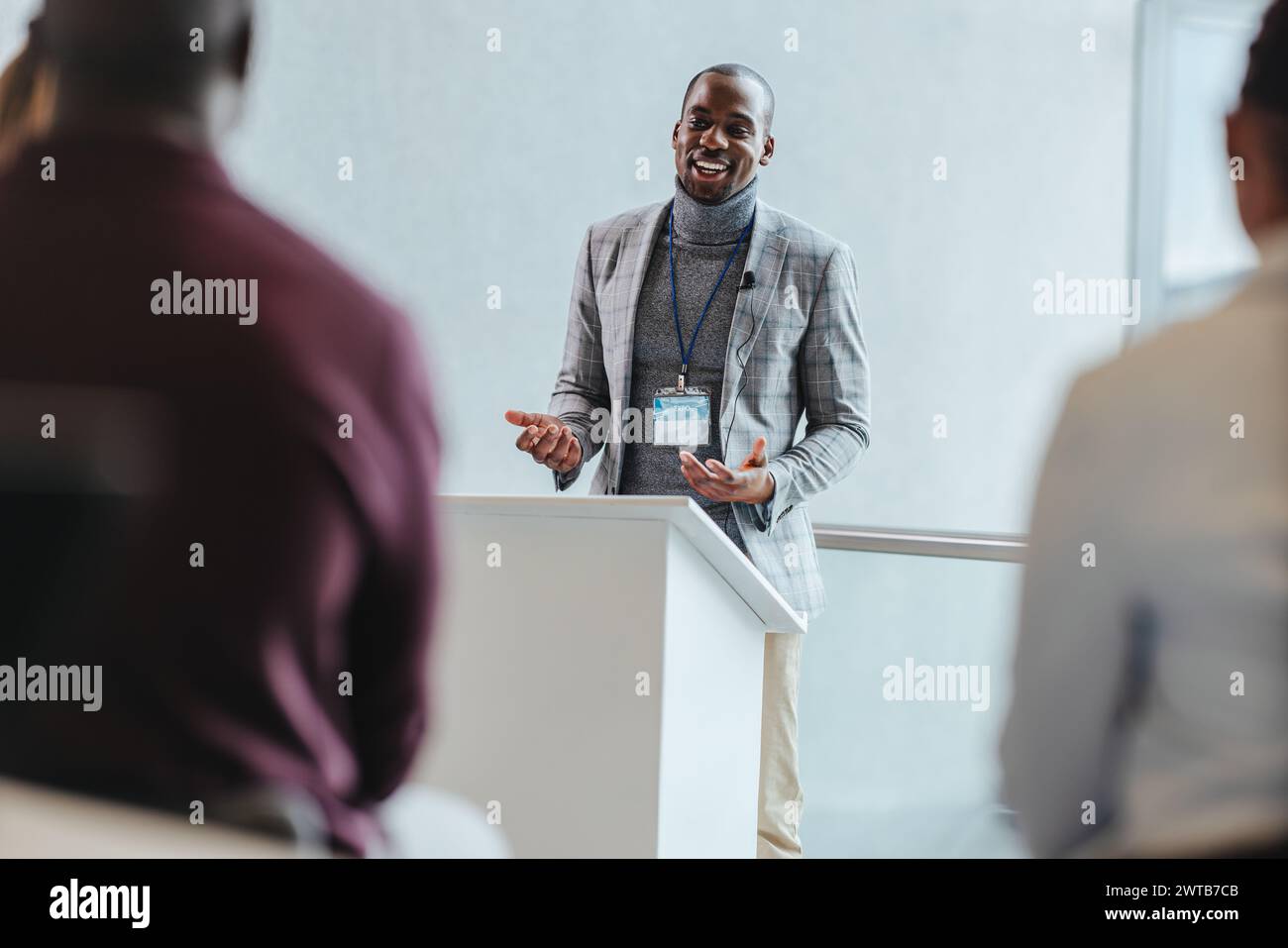 Ein professioneller männlicher Sprecher mit einem strahlenden Lächeln spricht ein Publikum bei einem Business Seminar an. Der Konferenzraum ist mit Tageslicht, Betonung, gefüllt Stockfoto