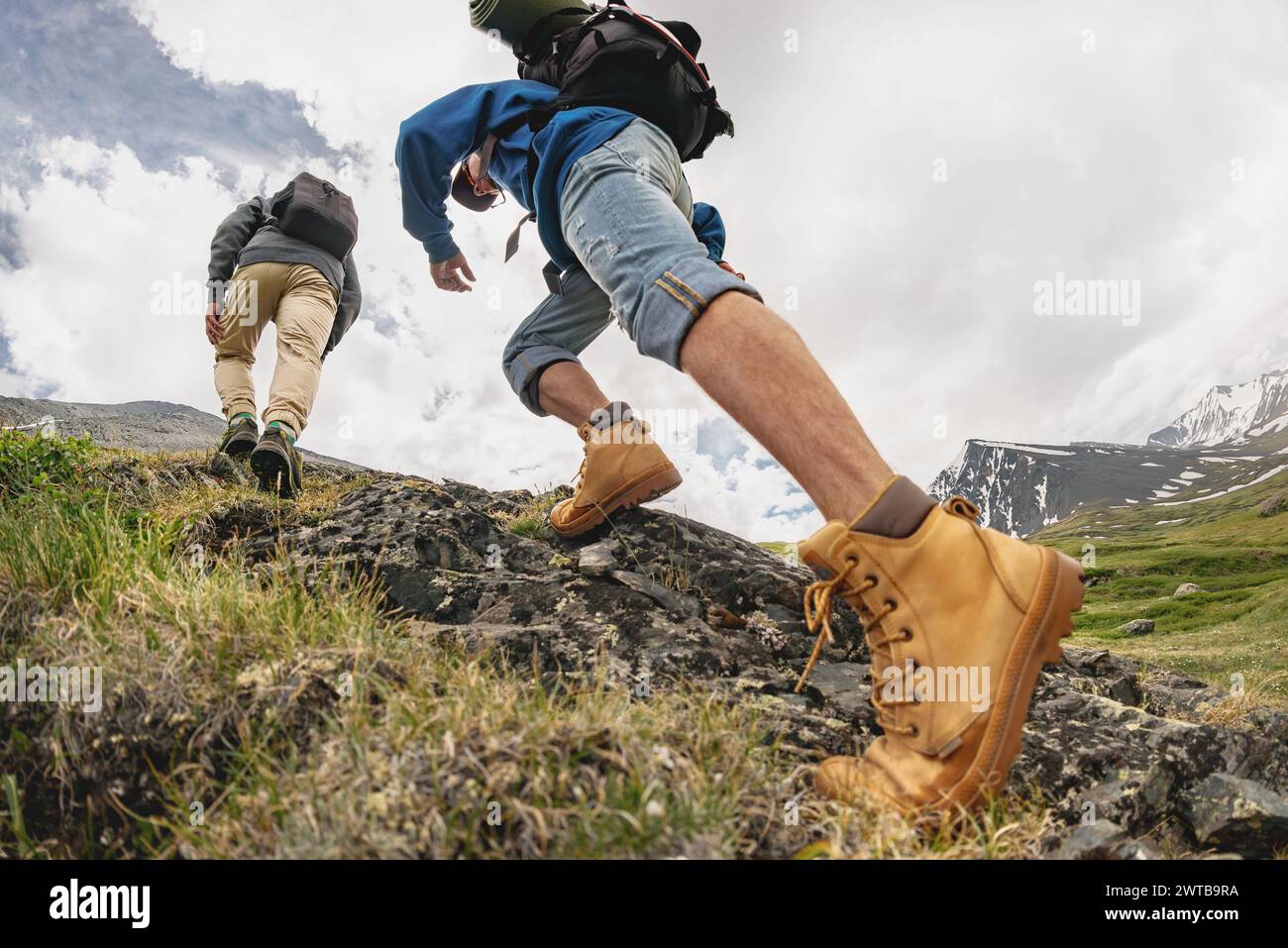 Zwei junge Wanderer mit Rucksäcken spazieren in den Bergen. Nahaufnahme von touristischen Beinen, die bergauf gehen Stockfoto