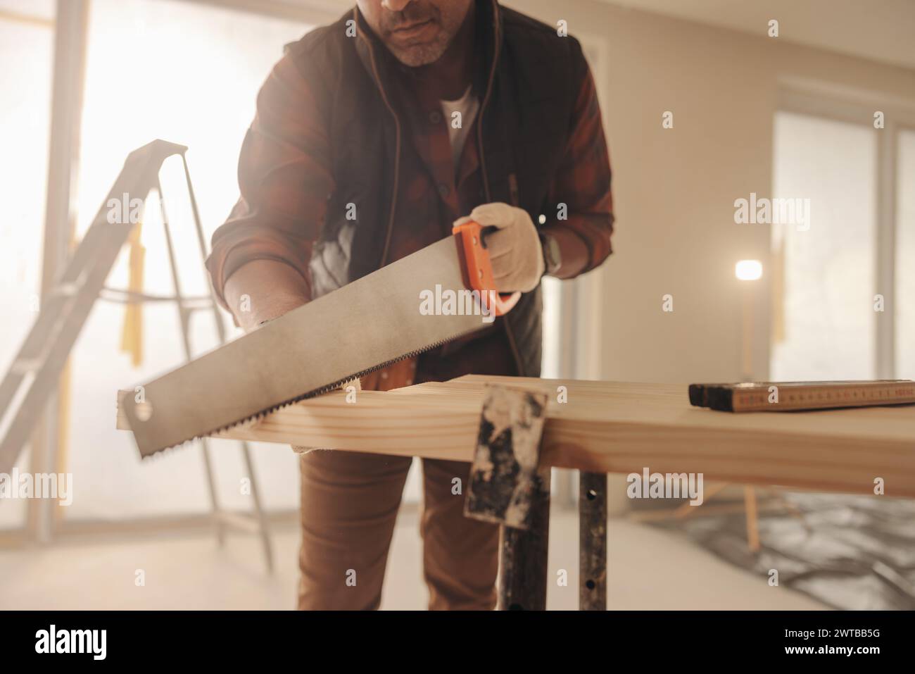 Zimmermann schneidet eine Holzdiele, während er an der Renovierung eines Hauses arbeitet. Bei der Arbeit im Innenbereich hilft dieser Facharbeiter bei der Modernisierung und Umgestaltung des Küchenbereichs Stockfoto
