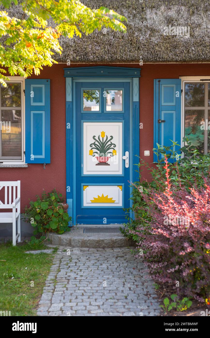 Farbenfrohe Eingangstür eines Strohdachhauses mit dekorativen Schnitzereien und Gemälden, Blumenmotiven, Sonne, blau und weiß bemalten Fenstern und Fensterläden Stockfoto