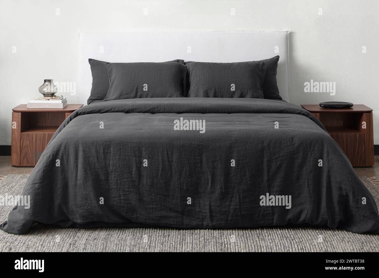 Komfortables Bett mit Kissen in modernem Zimmer. Innenarchitektur, Wandmotiv. Weißes Schlafzimmer mit Teppich und weißer Wand über bed.front Blick. Stockfoto