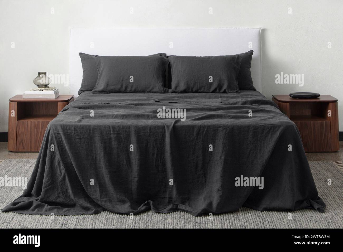 Komfortables Bett mit Kissen in modernem Zimmer. Innenarchitektur, Wandmotiv. Weißes Schlafzimmer mit Teppich und weißer Wand über bed.front Blick. Stockfoto