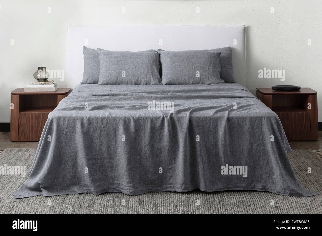 Komfortables Bett mit Kissen in modernem Zimmer. Innenarchitektur, Wandmotiv. Weißes Schlafzimmer mit Teppich und weißer Wand über bed.front Blick. Stockfoto