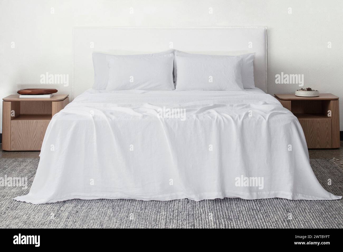 Komfortables Bett mit Kissen in modernem Zimmer. Innenarchitektur, Wandmotiv. Weißes Schlafzimmer mit Teppich und weißer Wand über bed.front Blick. Stockfoto