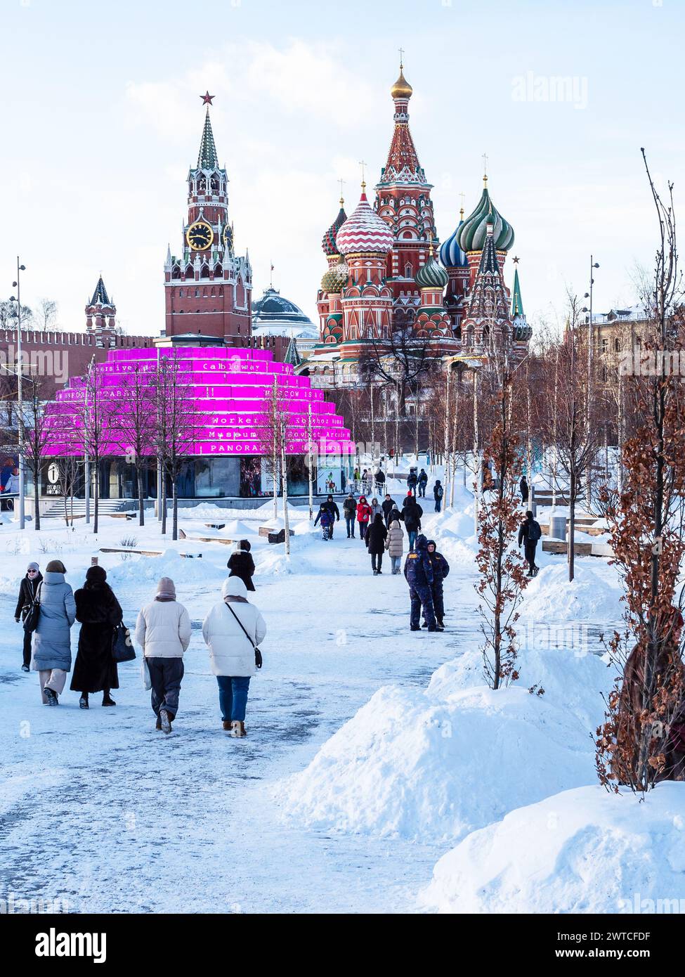 Moskau, Russland - 8. Februar 2024: Menschen auf verschneiten Wegen im öffentlichen Park der Stadt Sarjadje und Blick auf die Basilius-Kathedrale und die Kreml-Türme in Moskau Stockfoto